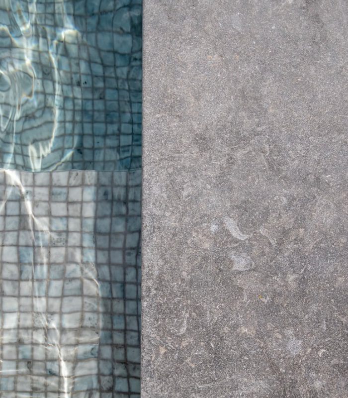 This image shows a close up of grey limestone pavers as pool coping.
