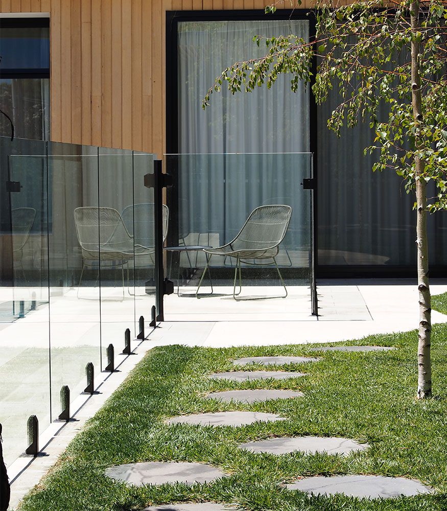 Stepping stones made from Brulee Limestone lead towards a tiled pool area with glass fencing.