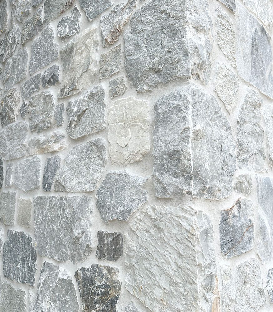 An external wall’s corner highlighting warm greys and dusty whites, featuring fractal-sized quartz and limestone deposits.