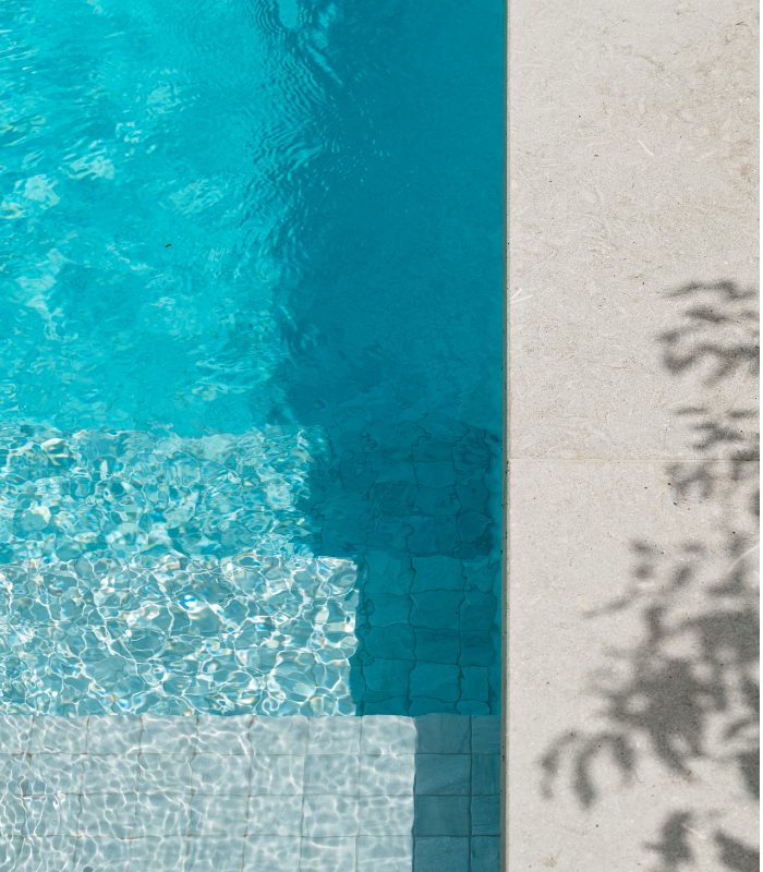A close up of Olivia Limestone pool tiles surrounding a blue pool.