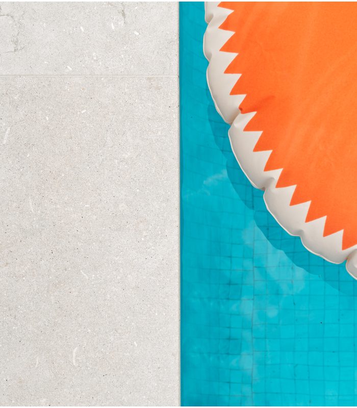 A close up of Olivia Limestone pool tiles surrounding a blue pool with an orange pool toy.
