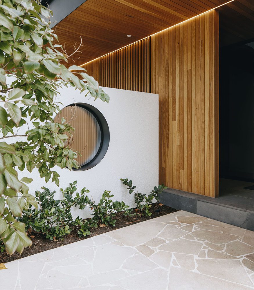 An image of a white feature wall behind a garden bed. A home's entrance to the right features wooden walls and ceilings.