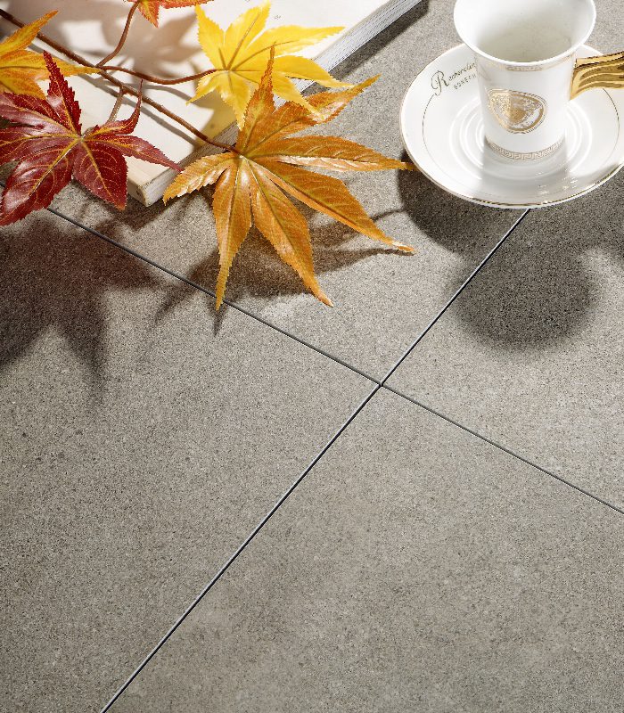 A close up of Nurage porcelain floor tiles. There’s a gold and white teacup and orange-leafed maple plant sitting on top of the tiles.