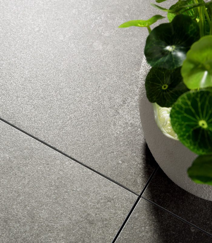 A close up of Nuage porcelain floor tiles. There’s a white pot on the floor with a green plant.