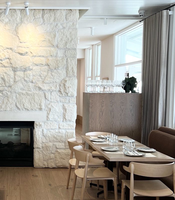 A beautiful Shell Limestone rustic fireplace feature. The white limestone cladding looks sleek next to a set wooden dining table, and a large wooden bar with wine glasses atop.
